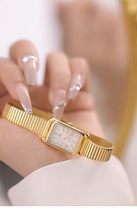 Close-up of golden rectangular watch with roman numerals and elastic metal band