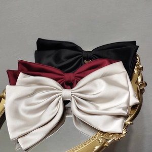 Three elegant satin bow hair clips in black, burgundy and cream on a golden tray