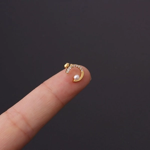 Macro shot of a tiny gold crescent ear stud with cubic zirconia and a small pearl