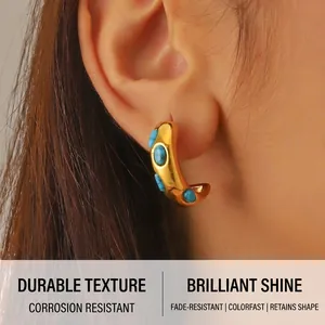 Close-up of a gold C-shaped hoop earring with turquoise beads on a model's ear