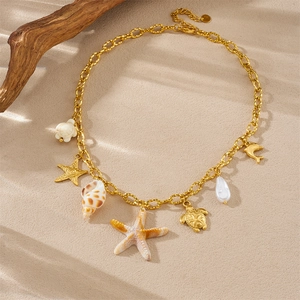 Flat lay of gold ocean charms necklace with starfish and turtle on sand beach
