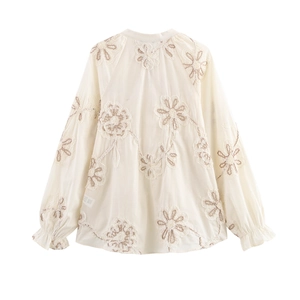 Close-up of floral embroidery detail and ruffled cuffs on cream long-sleeve blouse