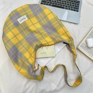 Detail of checkered canvas shoulder bag in yellow and purple on a white bed sheet