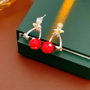 Detail of red cherry earrings with silver leaf and yellow zircon on a jewelry box