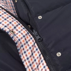 Close-up of navy blue quilted vest showing orange plaid lining, zipper, and metal snaps