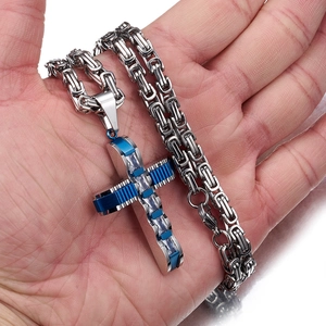 Detailansicht einer Hand mit einem silbernen und blauen Kreuzanhänger aus Edelstahl