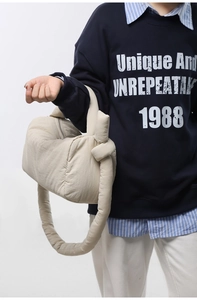 Detail of a puffy cream nylon shoulder bag featuring shoulder strap knot and silver zipper