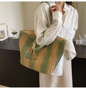 Detailed side view of a green striped straw tote bag with woven handles and tassel detail