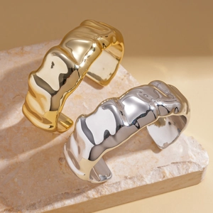 Minimalist gold and silver cuff bracelets with wavy water ripple texture on marble stone