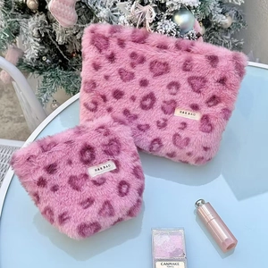 Detailed close-up of soft pink heart leopard faux fur cosmetic bag set on blue surface
