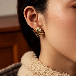 Close-up detail of gold diamond-shaped earrings with textured horizontal patterns on model