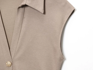 Detailansicht der khakifarbenen Twill-Struktur und goldener Metallknopf am Kragen