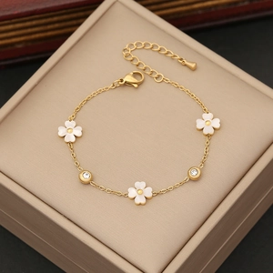 Detail of gold chain bracelet featuring white quatrefoil charms and inlaid clear zircons