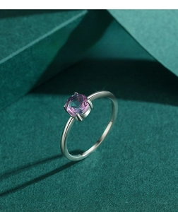Detail of round faceted purple gemstone set in four-claw silver band on green background