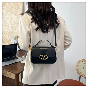 Detail of elegant black bag with golden oval clasp shown in a lifestyle office setting