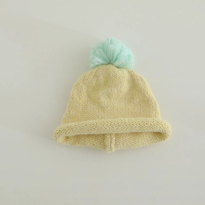 Detailed top view of child's yellow knitted hat featuring a large blue pom-pom accent