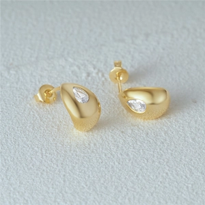 Macro shot of gold teardrop stud earrings with clear gemstone on white texture