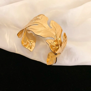 Detailed macro view of gold leaf pattern cuff bracelet on white silk fabric