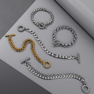 Dettaglio di bracciali in oro e argento con chiusura OT su uno sfondo grigio