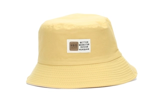 Detailed view of the yellow cotton bucket hat with a woven text patch on a white background