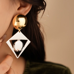 Close-up of geometric earrings with gold spheres and silver hollow diamond shapes