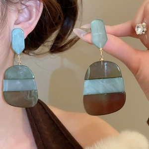 Detail of oval acetate drop earrings with green and brown marble patterns and gold accents