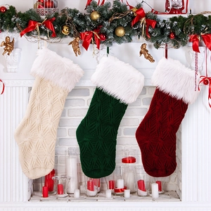 Three cable-knit Christmas stockings in beige, green, and red hanging on a fireplace mantel
