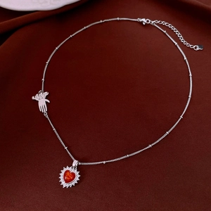 Detail of silver necklace with red heart pendant and small palm charm on red silk