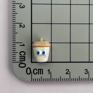 Macro shot of mini resin baby bottle charm with eyes on measuring mat showing 1.5cm size