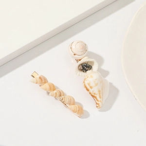 Macro shot of two shell hair clips featuring natural conch and cowrie on white surface