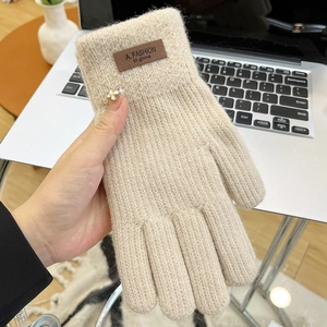 Close-up of beige knit gloves with brown leather fashion label on the wrist cuff