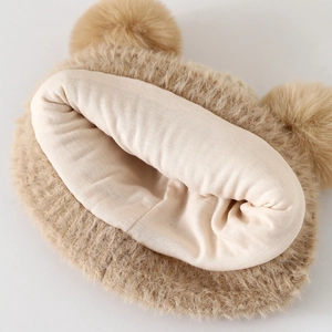 Dettaglio del cappello in peluche marrone per neonati con doppi pompon e morbida fodera in cotone