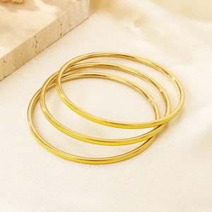 Detailed close-up of three polished gold stackable bangles on a textured surface