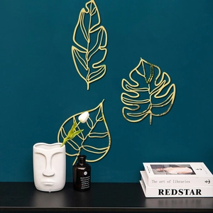 Détail de trois décorations murales en feuilles de métal doré sur un mur sarcelle foncé