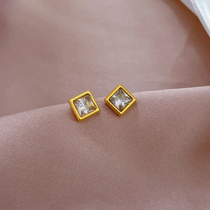 Detailed macro view of square gold titanium stud earrings with clear zircon on purple silk