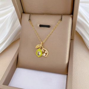 Macro view of gold fruit-shaped pendant with green enamel, white pearls, and crystals