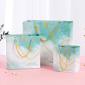 Teal watercolor paper gift bags with gold line patterns and braided handles in three sizes