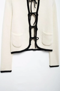 Détail du cardigan en maille avec nœuds noirs et passepoil contrasté sur poches