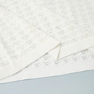 Detail of white knitted fabric featuring diamond hollow-out pattern and ribbed edge finish