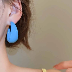 Close-up of bright sky blue C-shaped acrylic hoop earrings worn by a model