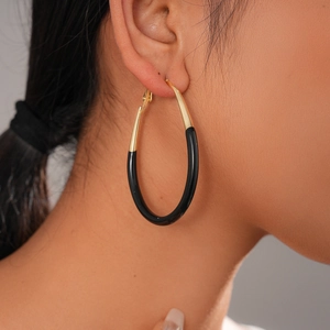 Close-up of gold and black enamel oval hoop earrings worn by a female model