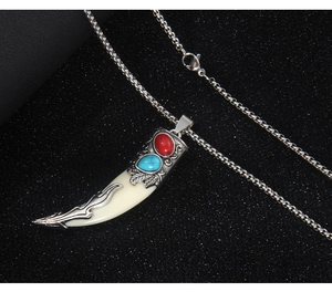 Detail of silver wolf tooth pendant with red and blue gemstones on a black background