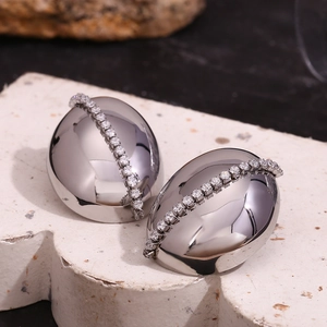 Macro shot of silver-colored oval earrings with white zircons on a white stone base