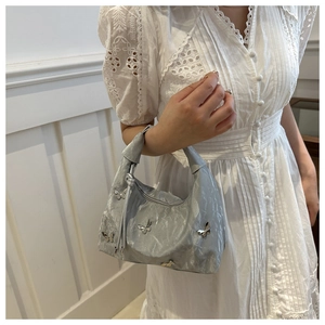 Close-up of a silver crescent handbag with metallic butterfly rivets on soft fabric