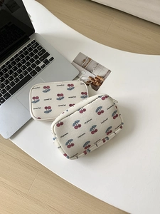 Detail of canvas cherry makeup bags on a white desk with a laptop for size scale
