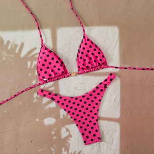 Detailed flat lay of pink polka dot bikini with a golden sun metal buckle on sand background