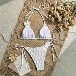 Flat lay of white two-piece ribbed bikini set with decorative dry flowers and a summer mat