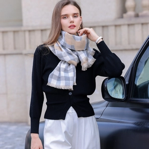 Grey and beige plaid scarf with H-pattern and tassels worn by a model in outdoor setting