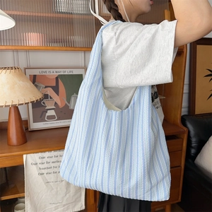 Detailed texture of blue striped canvas tote bag on a model's shoulder in cozy room