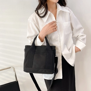 Minimalist black canvas tote bag with adjustable shoulder strap worn by a model